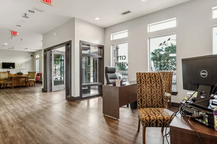 leasing office with large windows letting in a lot of light, a desk, comfortable seating, and hardwood floors