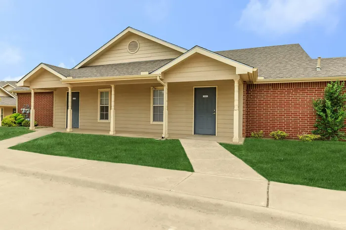 the front view of a couple of apartments, situated with a nice front patio and a walkway next to lush green grass