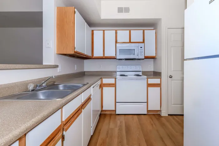 Spacious kitchen with white appliances, double sink, and wood-accented cabinetry at Willowbend Apartments in San Antonio, TX.