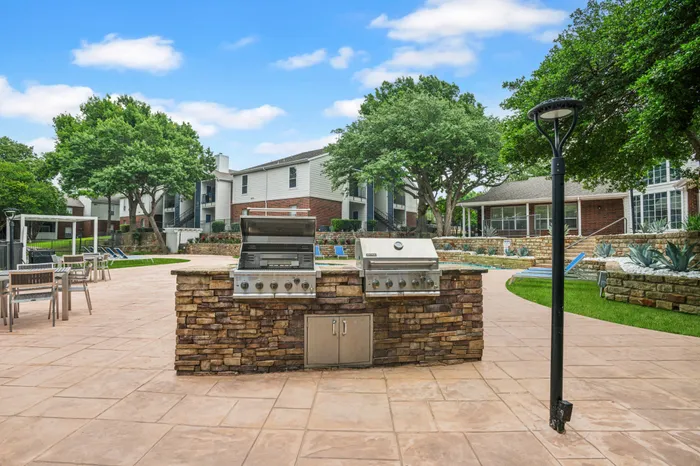 Outdoor grilling stations with stone accents, located by the pool area at a Plano, TX apartment community.