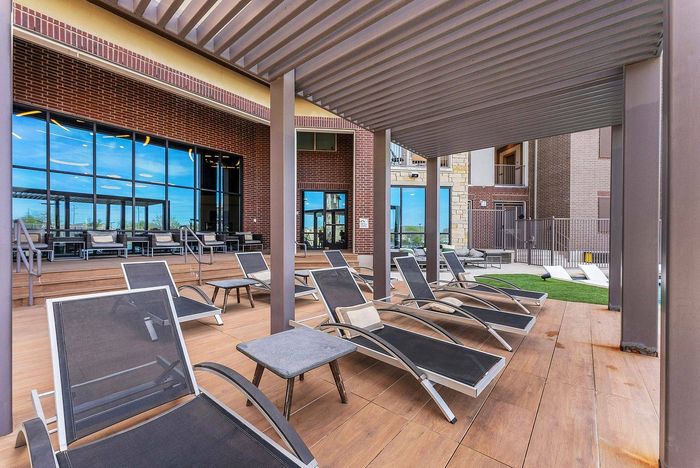 Shaded outdoor lounge area with modern black chaise chairs at Discovery Park Apartments in Denton, TX