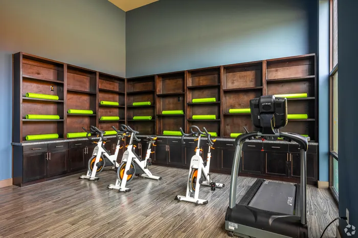 Spin studio with stationary bikes, a treadmill, and yoga mats on built-in wooden shelving at Discovery Park Apartments.