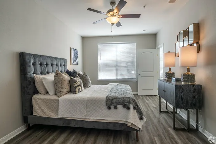 Elegant bedroom with tufted headboard and ceiling fan at Towne West Apartments in Houston