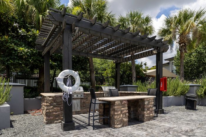 poolside BBQ grills situated under a modern pergola and next to multiple tables and chairs