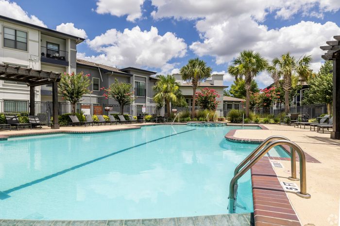 resort-style swimming pool surrounded by a wide cement walkway and shaded seating