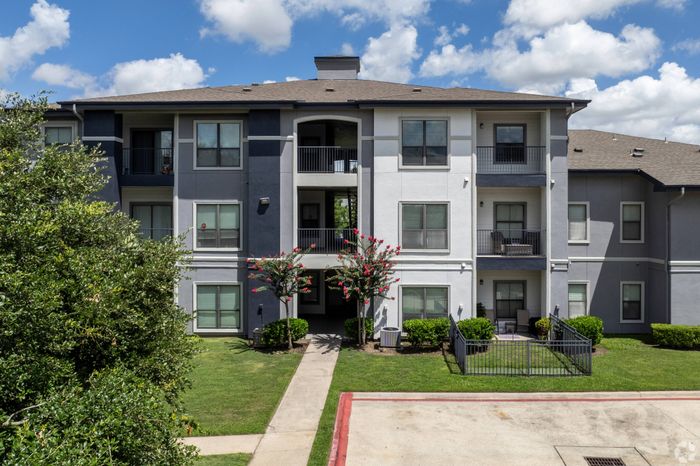 sidewalk leading to apartment buildings that are surrounded by lush green grass