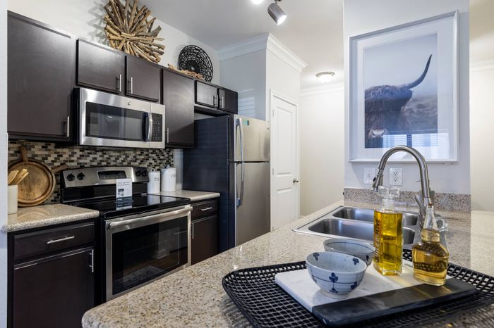 beautiful modern kitchen with luxurious layout and long bar, stainless steep appliances, and dark cabinets
