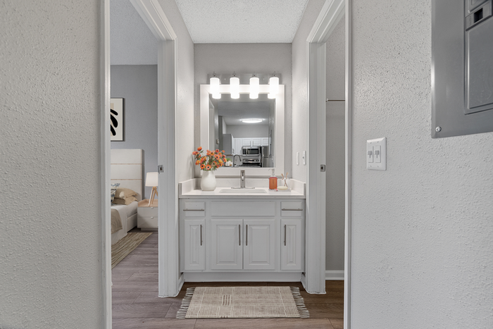 Bathroom with quartzs counters, large mirror, vanity lighting, and white cabinetry