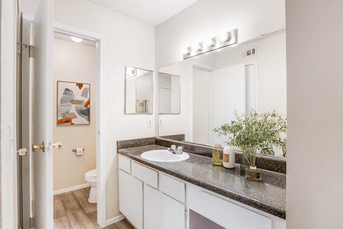 Bathroom with granite counters, large mirror, vanity lighting, and white cabinetry