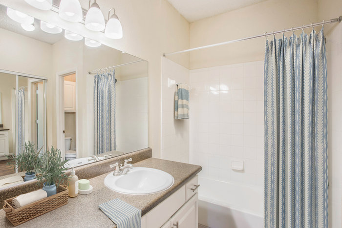 Bathroom with granite counters, mirror, vanity lighting, and brown cabinetry