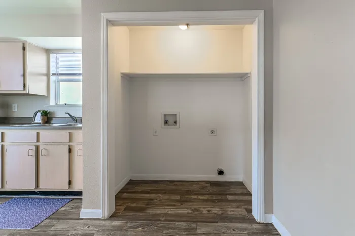 a room with hardwood floors, a washer and dryer, and a view of the kitchen which contains black appliances