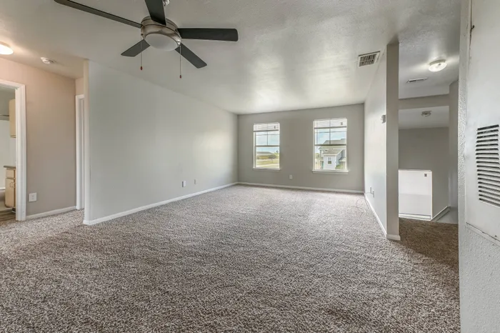 a plush carpeted living room with two windows, a ceiling fan, and a large floor perfect for furniture