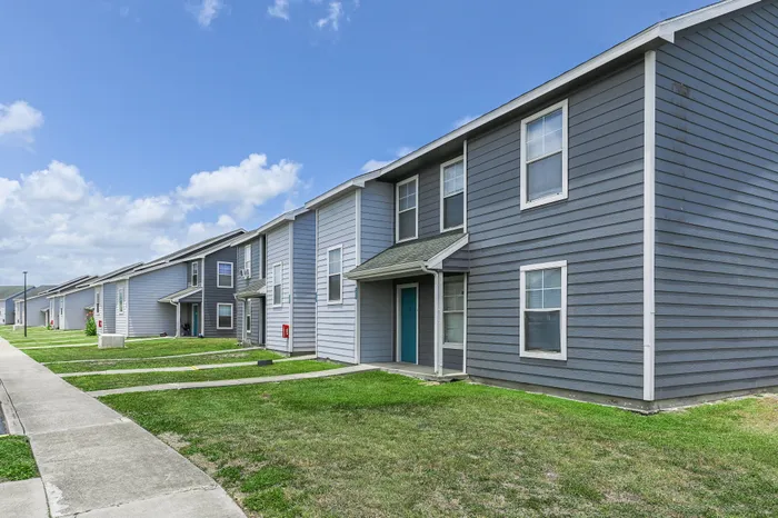 a charming apartment building with sidewalks leading from the many front doors leading to a larger sidewalk that passes lush green grass