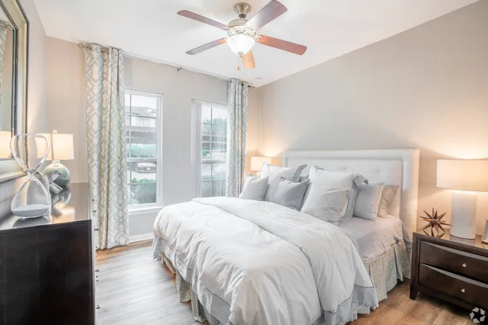 Cozy bedroom with large windows, ceiling fan, and neutral décor at Amalfi at Tuscan Lakes in League City, TX.