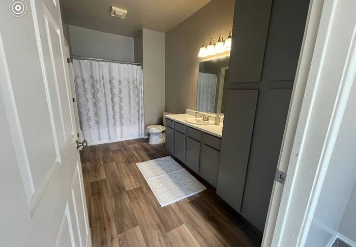 a clean bathroom with a white door, hardwood flooring, and a white bathtub