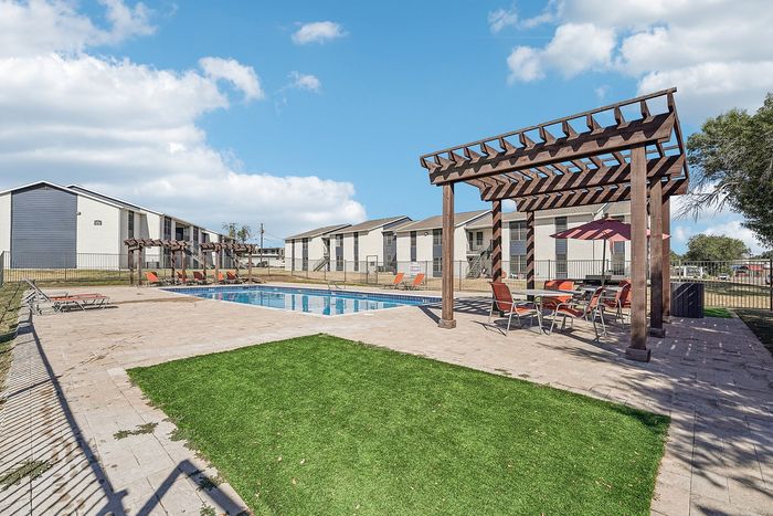 Pergola-covered seating area with dining tables and umbrellas next to a pool in a Waco, TX apartment community.