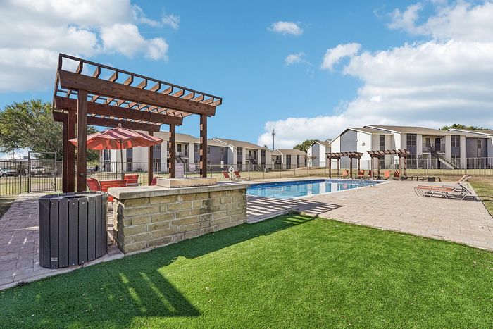 Pergola-covered seating area with dining tables and umbrellas next to a pool in a Waco, TX apartment community.