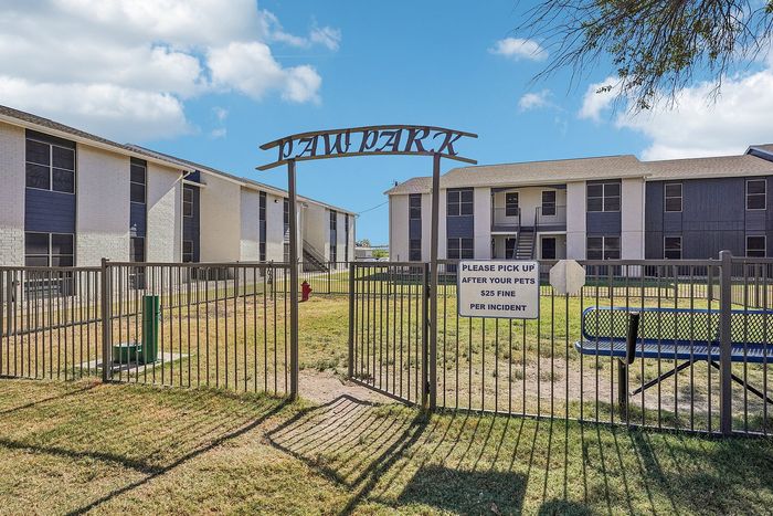 Fenced dog park with lush green grass and shaded areas in a pet-friendly apartment community in Waco, TX.