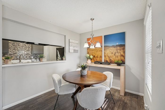 Dining area with a modern round table, upholstered chairs, and wall art, located near a bright window in a Waco, TX apartment.