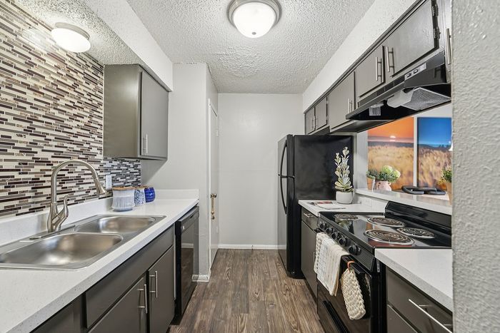 Modern kitchen in a Waco, TX apartment featuring sleek dark cabinetry, mosaic tile backsplash, stainless steel sink, and updated appliances.
