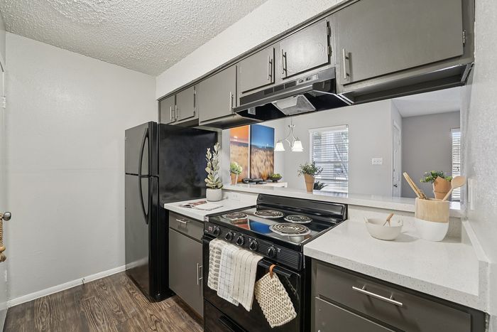 Modern kitchen in a Waco, TX apartment featuring sleek dark cabinetry, mosaic tile backsplash, stainless steel sink, and updated appliances.