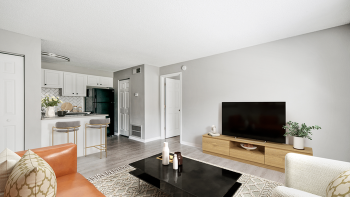 Livingroom with hardwood floor cream rug, black coffee table, orange leather couch, flat screen TV, kitchen, barstools