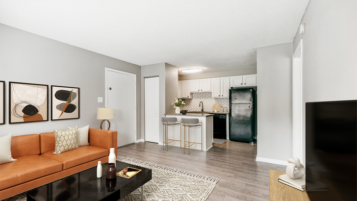 Livingroom with hardwood floor cream rug, black coffee table, orange leather couch, flat screen TV, kitchen, barstools