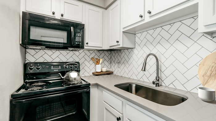 Black appliances, white cabinetry, white tile backsplash, undermount gooseneck faucet