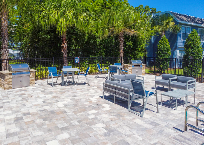 Pool griling area with grill, gray cushioned patio furniture, blue chairs and gray tables