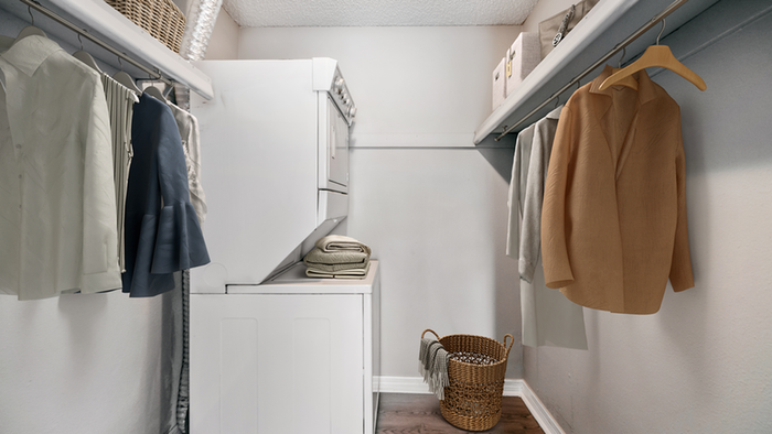 Laundry room with stacked washer and dryer, wooden floor, clothes hanging, baskets on top shelf
