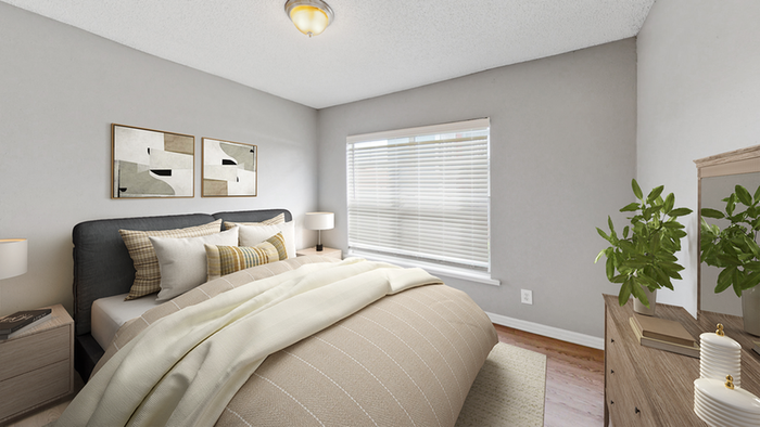 Bedroom with hardwood flooring, tan rug, wood dresser and end table, table lamp, queen size bedding, wall art