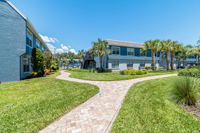 Exterior of apartment with lush landscaping,  palm trees, sidewalk andlandscaping