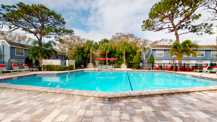 Pool with lounge chairs red umbrellas, exterior of apartment buildings, trees