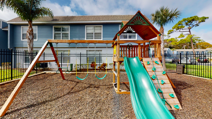 Playground with slide, swings, and climbing wall, surrounded by a fence.