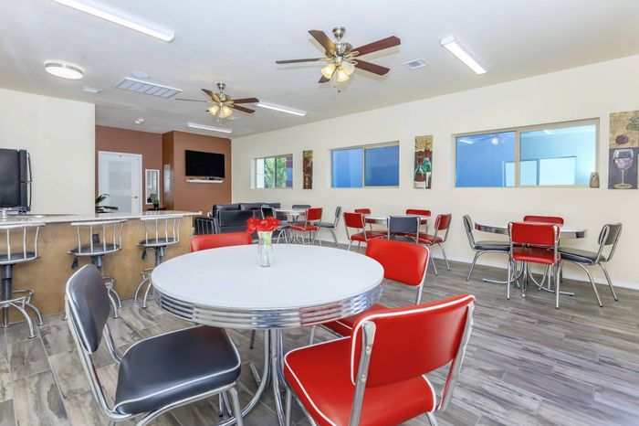 Community room with tables, red chairs, lounge seating, and ceiling fans at Bella Vista Place Apartments