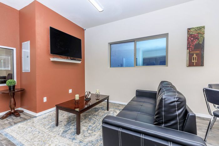 Resident lounge with black sofa, coffee table, wall-mounted TV, and accent wall at Bella Vista Place