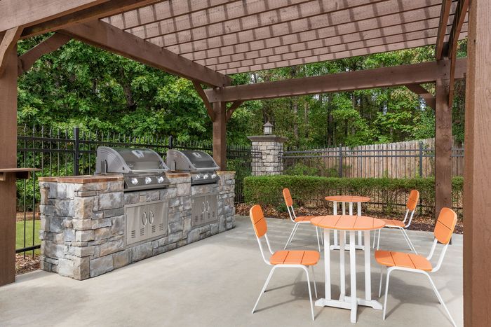 Charming outdoor picnic area with sleek stone grills and vibrant orange seating under a stylish pergola.