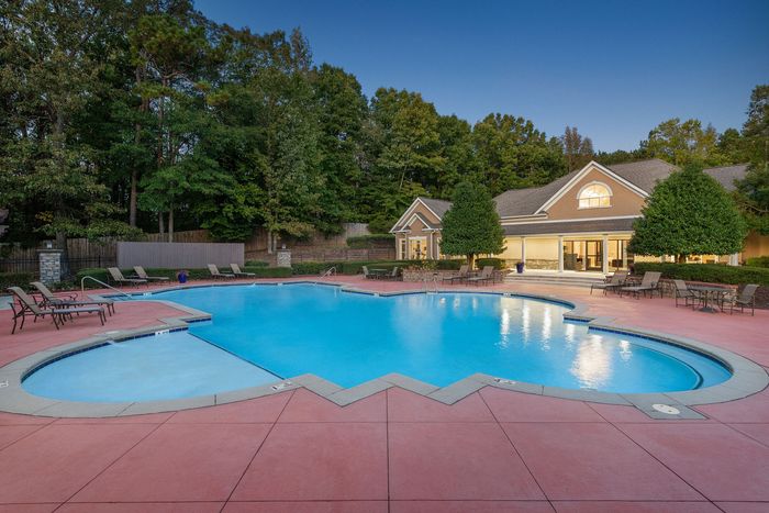 Inviting residential pool with surrounding lounge chairs, nestled in lush greenery and adjacent to a charming clubhouse.