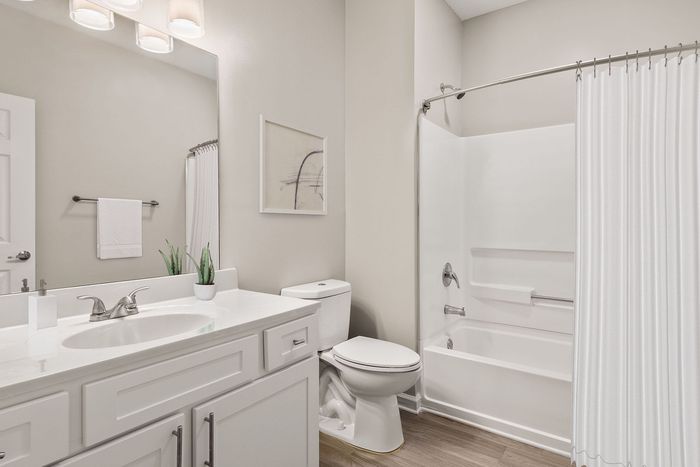 Elegant bathroom featuring sleek white cabinetry, a modern sink, and a stylish bathtub with curtain, highlighted by soft lighting and tasteful decor.