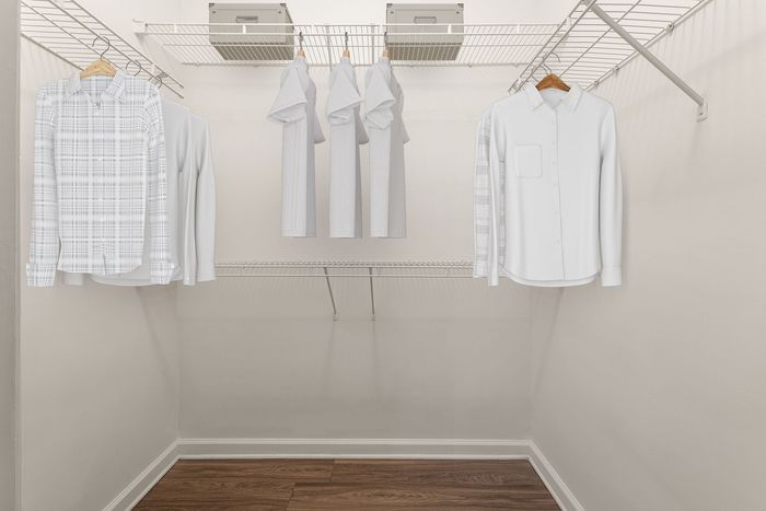 Spacious walk-in closet with sleek wooden floors and an organized wire shelving system, showcasing ample storage with hanging shirts and folded clothes.