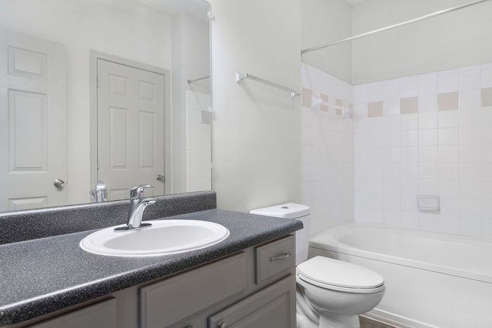 Bright and modern bathroom with sleek vanity, elegant faucet, and a tub with pristine white tile accents.