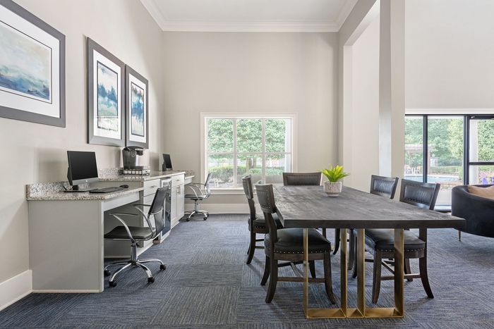 Modern communal office space with sleek computers, elegant art pieces, a large window with garden views, and a stylish conference table.