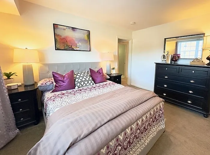 Cozy and elegant bedroom featuring a plush bed with vibrant pillows, stylish decor, and warm lighting creating a serene atmosphere.