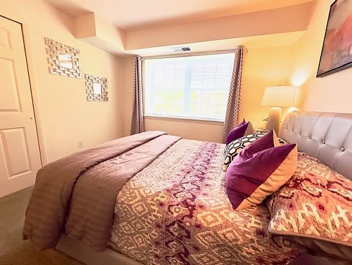 Inviting bedroom with plush bedding, stylish decor, and abundant natural light through a large window.