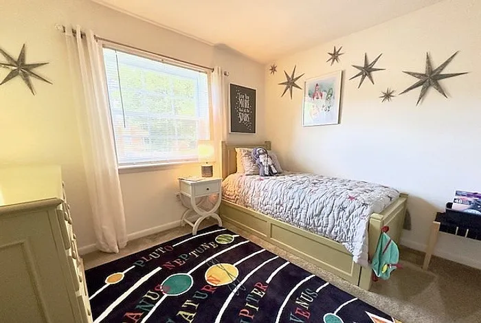 Charming child's bedroom featuring a cozy bed, playful star decor, and a colorful planetary-themed rug, illuminated by natural light from a large window.