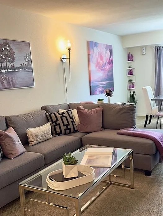 Chic and cozy living room with modern gray sofa, plush decorative pillows, elegant glass coffee table, and artistic wall decor. Perfect for relaxing and entertaining.
