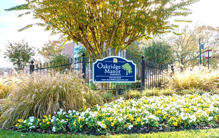 Charming Oakridge Manor sign surrounded by vibrant flowers and lush greenery under a sunny sky.