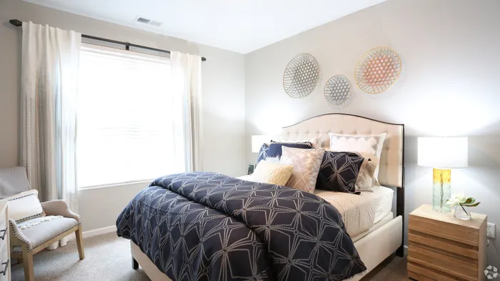 Inviting bedroom with elegant navy blue bedding, soft gray walls, and tasteful decor under natural light.