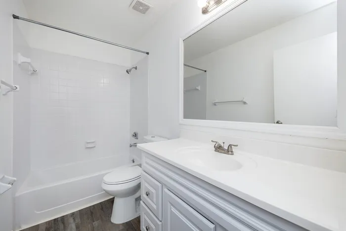 Renovated bathroom with luxury vinyl wood flooring and white cabinetry.