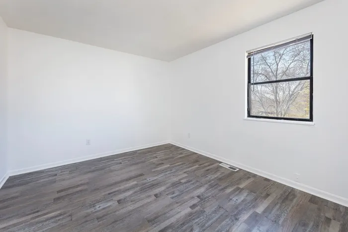 Spacious bedroom with vinyl wood flooring and large windows.